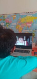 A child is sitting in front of a laptop, watching an animated