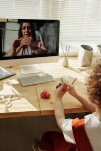A child engaged in an online crafting lesson, following a tutorial on a computer screen while shaping colorful clay.